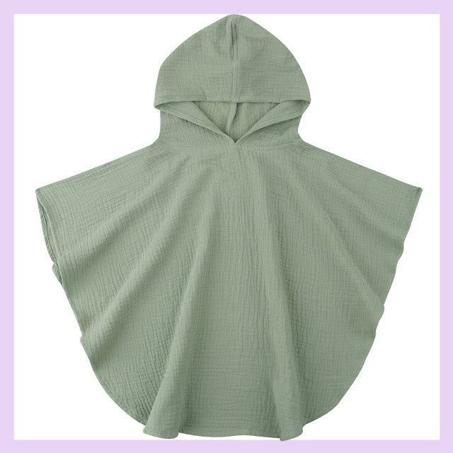 Green hooded poncho with a textured fabric, displayed against a light purple frame. The design is simple with a curved hem and short sleeves, creating a casual and cozy appearance.