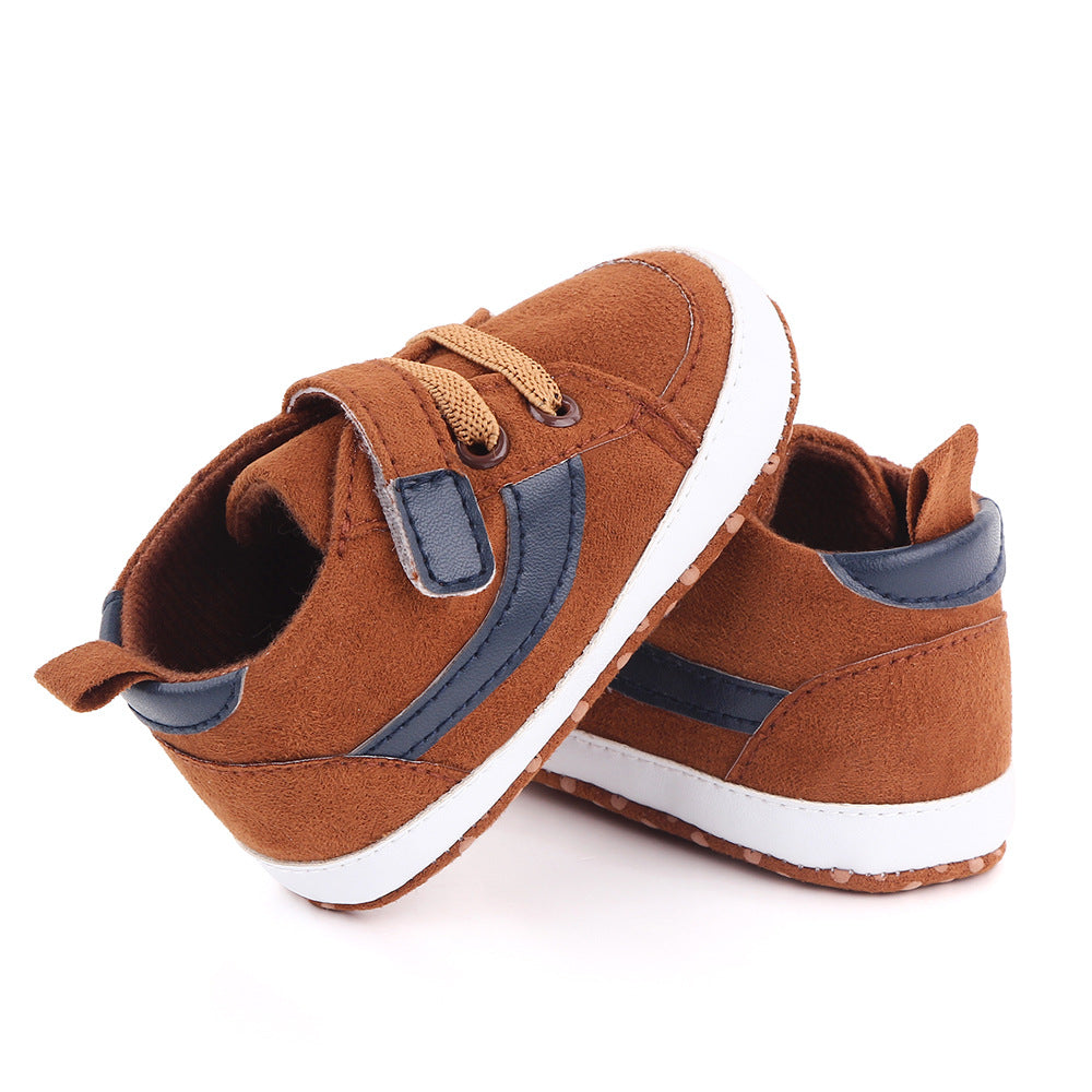 Brown baby sneakers with tan laces and blue accents, featuring white soles and cushioned interior. One shoe is leaning against the other on a white background.