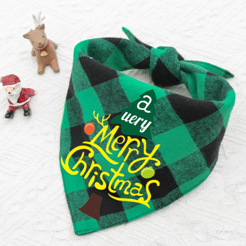 Green and black plaid pet bandana with "A Very Merry Christmas" text, placed on a white surface. Small reindeer and Santa figurines are in the background.
