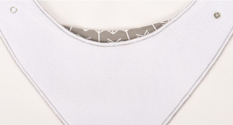 Close-up of a white baby bib with a curved gray fabric insert featuring a white geometric pattern. Two metal snap buttons are visible on the edges against a light background.