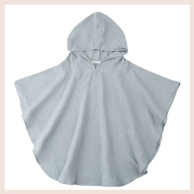 Light blue hooded poncho made of soft, textured fabric, displayed flat against a neutral background. Designed for comfort and style, featuring wide sleeves and a loose fit.