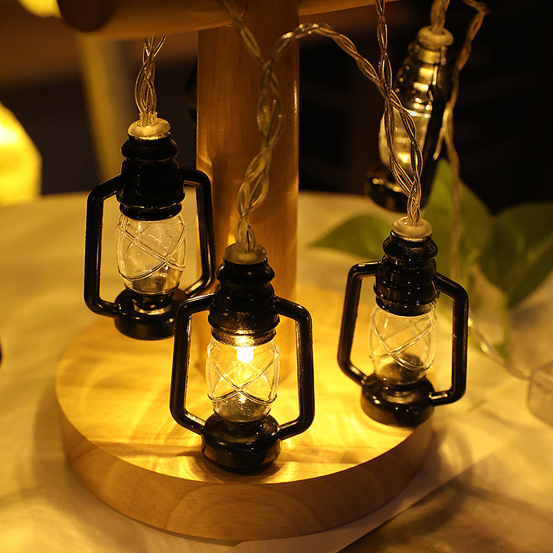 String lights resembling mini lanterns hang on a wooden pole, casting a warm glow on the table surface. A green leaf is visible in the background, adding a touch of nature.