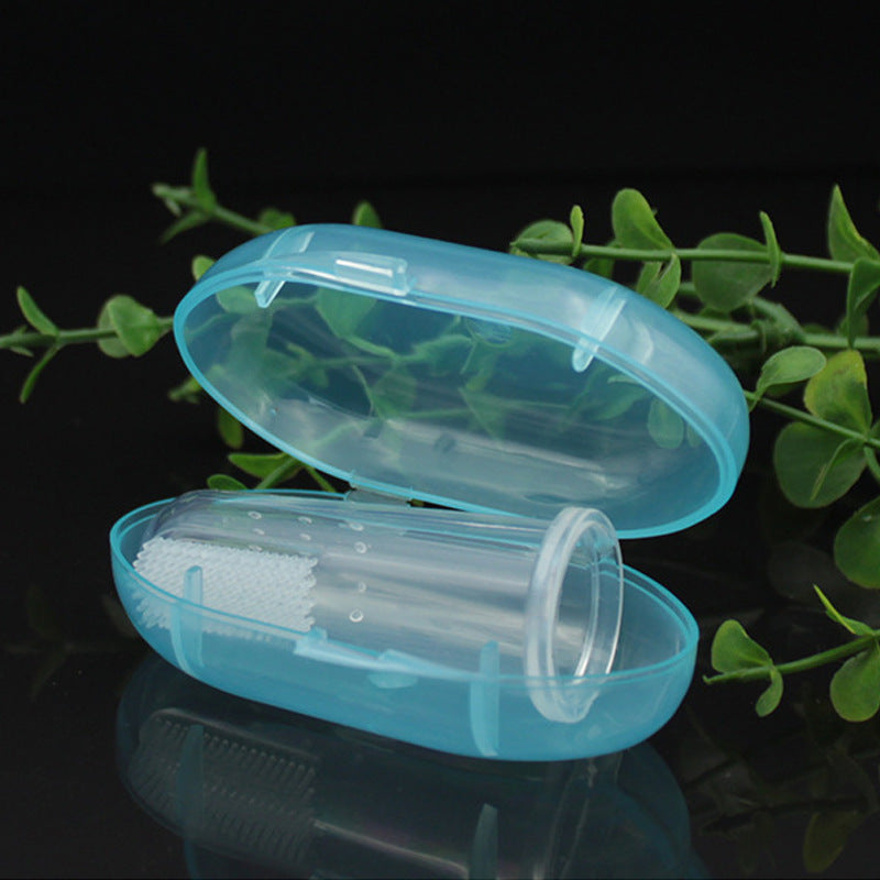 Clear finger toothbrush in an open blue case on a black reflective surface, with green leaves in the background.