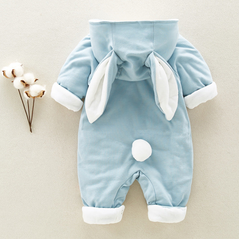 A blue baby onesie with bunny ears on the hood and a fluffy tail on the back, placed next to a cotton branch. The cuffs and ears are lined with white fabric.