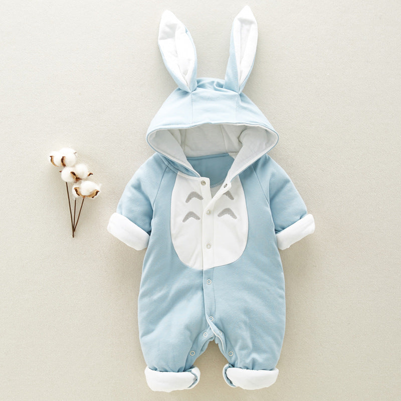 A cute baby jumpsuit with bunny ears and a Totoro design on the chest, in light blue and white. It's displayed on a beige background beside cotton branches.