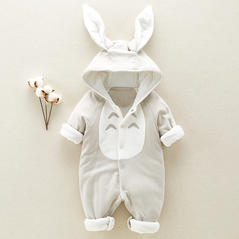 Gray baby onesie with a hood featuring bunny ears, buttoned front, and a cute face design on the chest. It lies on a beige surface next to sprigs of cotton flowers.