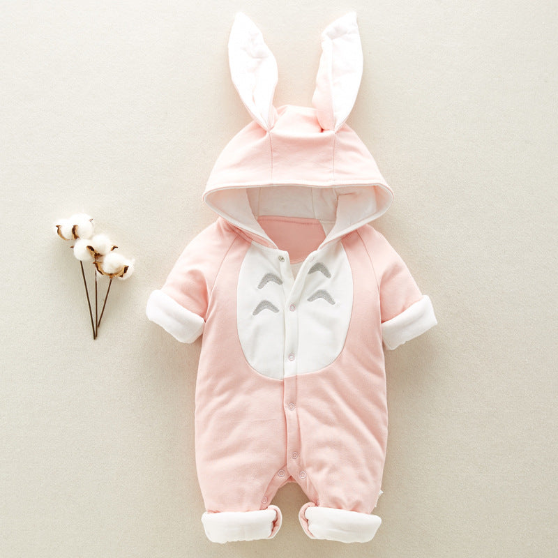 Pink baby romper with bunny ears on hood, white chest with smiling design, and rolled cuffs. Next to a small branch with cotton blooms on a beige background.