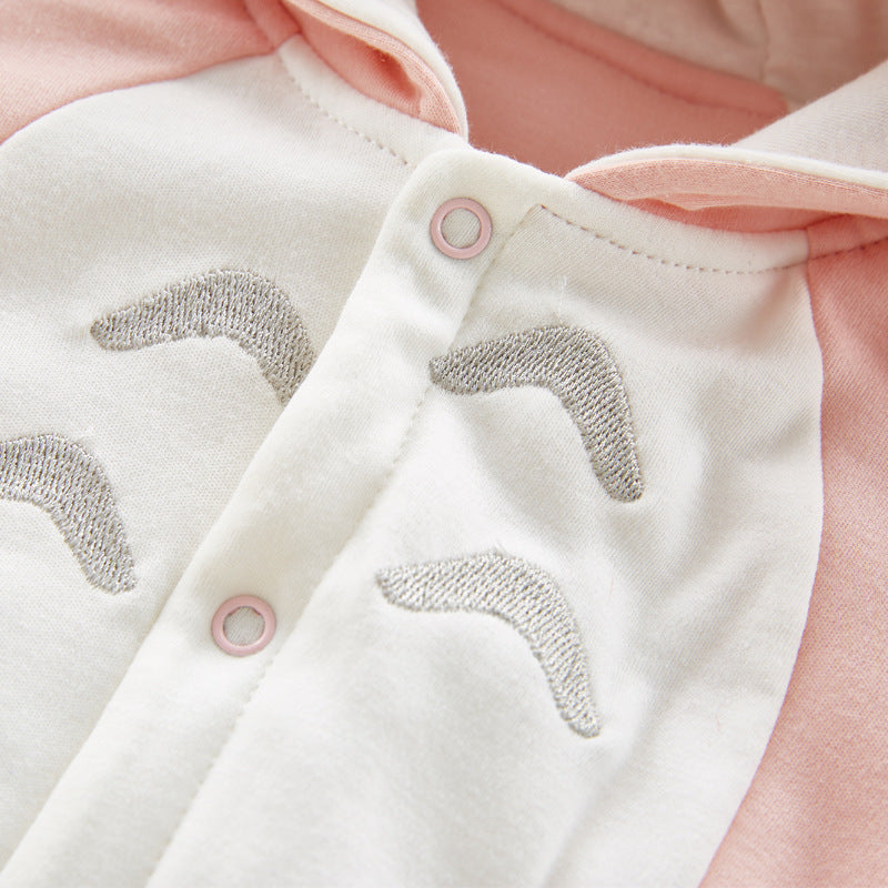 Close-up of a pink and white fabric with silver embroidered patterns and snap buttons. The design includes curved lines and soft textures, with a glimpse of a hoodie.