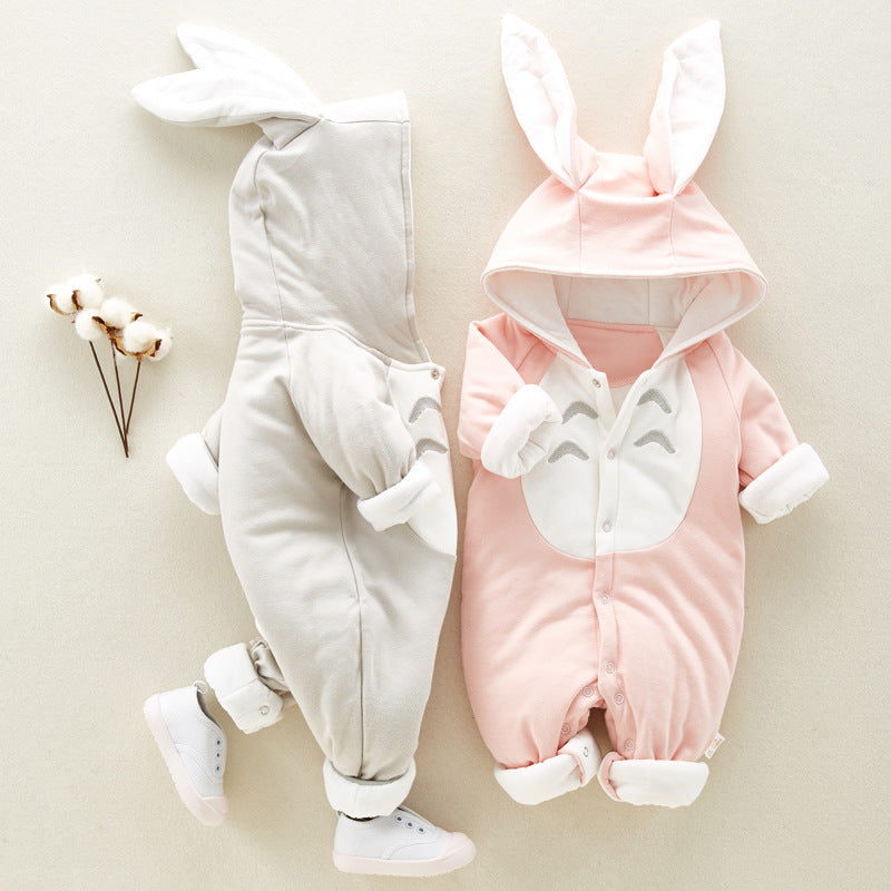 Two animal-shaped baby onesies, one gray and one pink, each with cartoonish faces and rabbit ears. A small branch of cotton lies nearby on a light background.