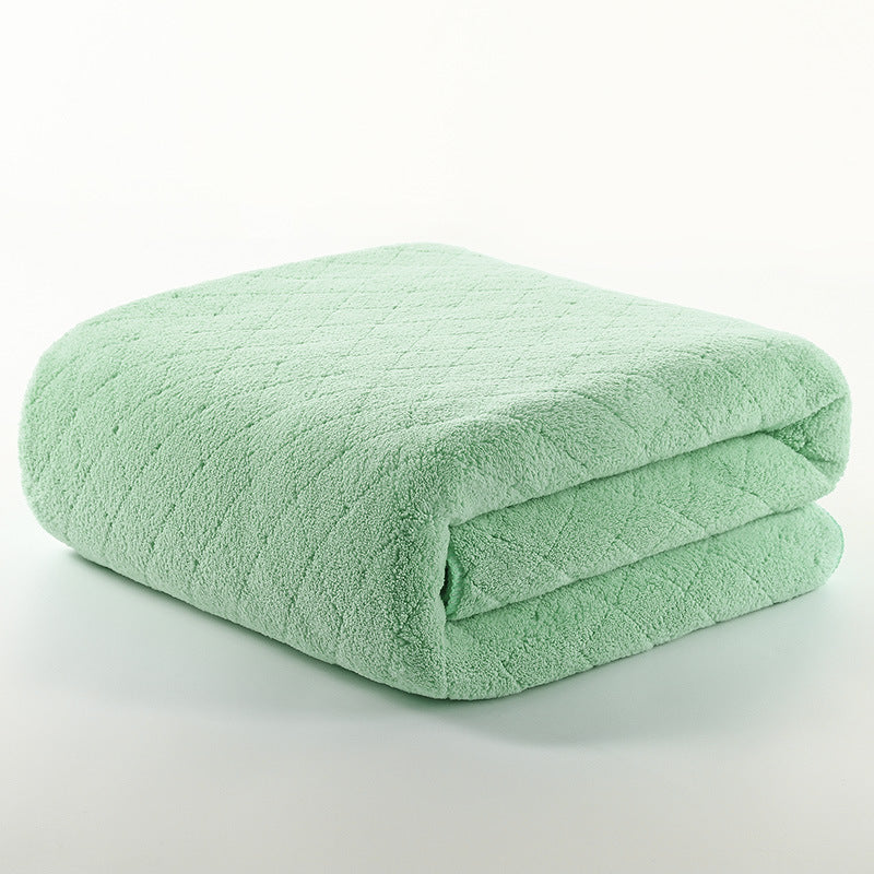 A soft, light green folded blanket with a diamond pattern texture lies on a plain white surface, showing its plush and cozy material.