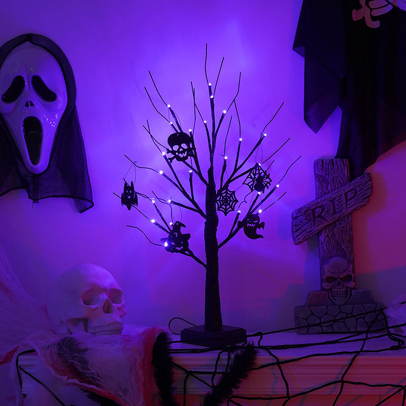 A room with a Halloween theme features a purple-lit tree adorned with skull and spider ornaments, a scream mask, a skull decor on a mantel, and a tombstone marked “RIP.”