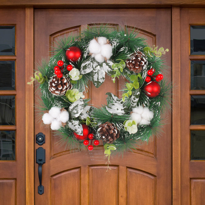 Festive wreath on a wooden door, adorned with red ornaments, pine cones, cotton, frosted leaves, and greenery, creating a cheerful holiday display.
