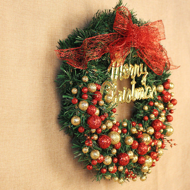 Festive Christmas wreath with glittery red and gold baubles, a "Merry Christmas" sign, and a large red bow, hung on a textured, light brown wall.