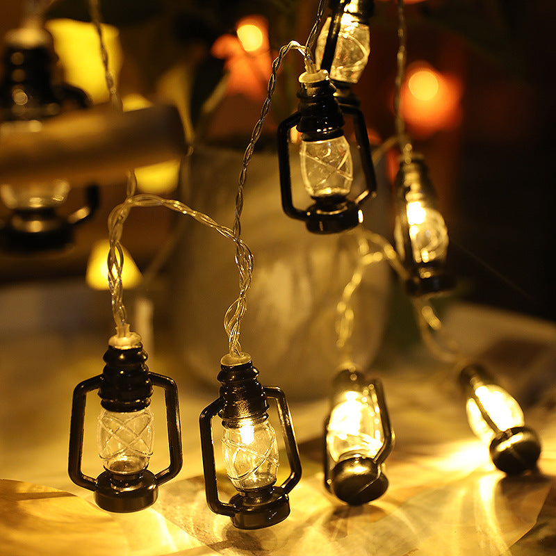 String lights with mini lantern designs emit a warm glow, hanging decoratively on a surface. The scene has a cozy ambiance with blurred warm lights in the background.