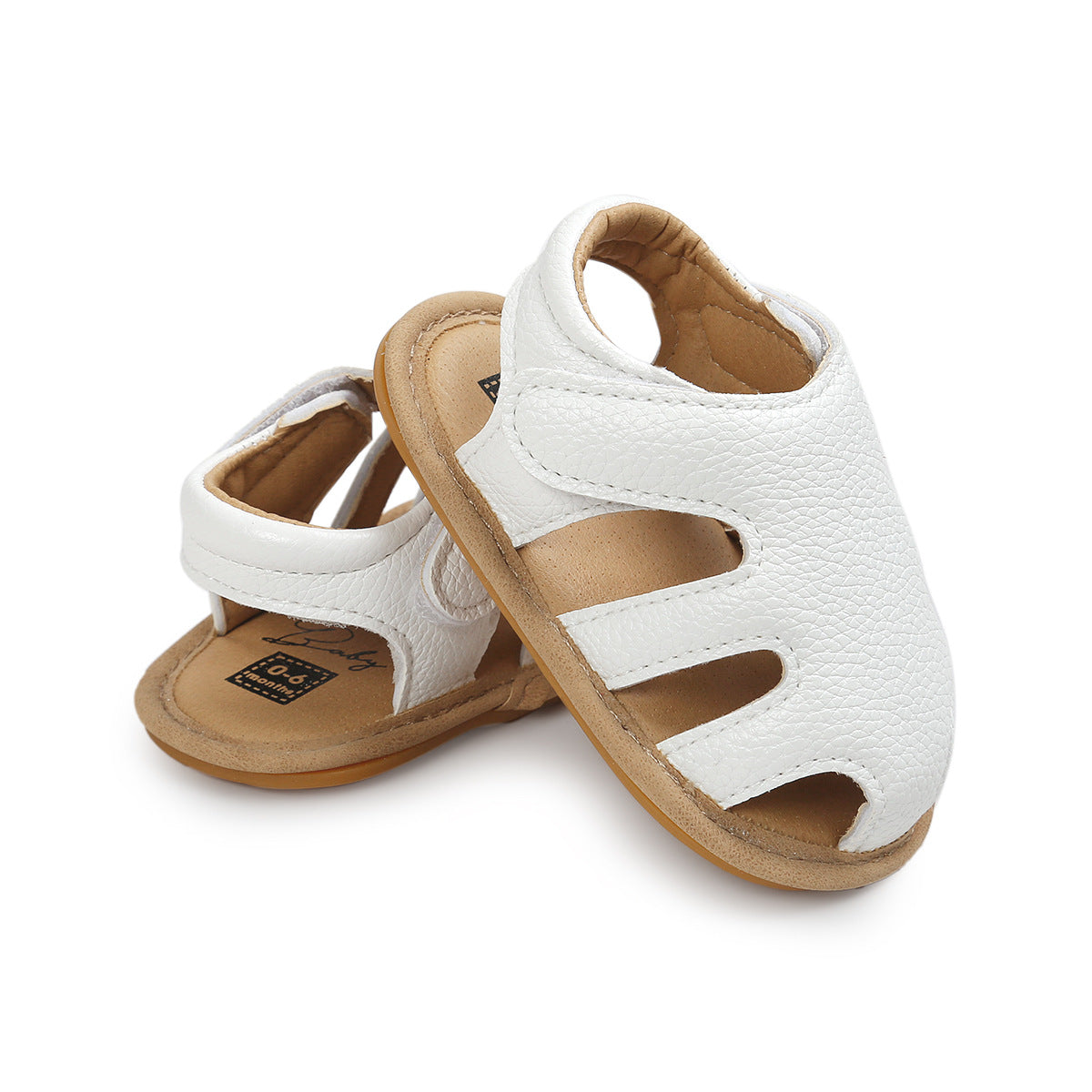 White baby sandals with cutout design and tan soles, featuring a soft texture and ankle strap. Positioned overlapping on a white background.