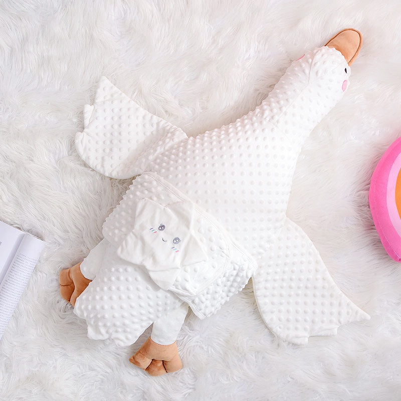 White textured plush duck blanket with tan feet and a cute face design, lying on a fluffy white surface. There's a pink object partially visible on the right.