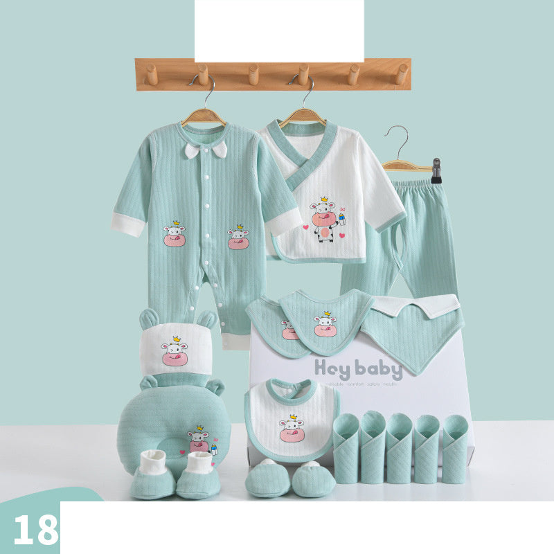 A display of mint green and white baby clothes with cute cow prints, including a onesie, top, pants, bibs, mittens, and booties, neatly arranged with matching accessories.