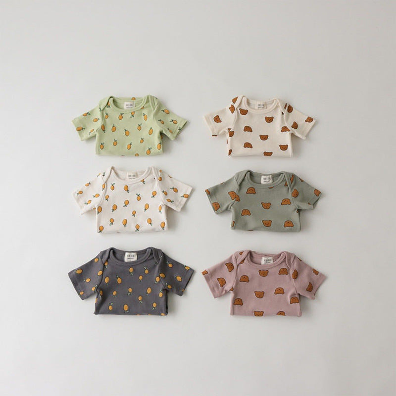 Six baby shirts displayed on a flat surface, each with adorable prints: green and white with fruit, white with bears, gray with fruit, and gray and purple with animal faces.