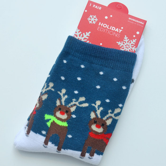 Blue holiday socks featuring reindeer with red and green scarves in falling snow. Labeled "Holiday Editions" on red packaging with snowflakes.