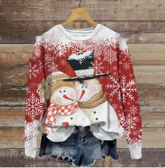 Festive sweater with two smiling snowmen, one with a red scarf, the other with a top hat. Red background adorned with white snowflakes. Hangs over denim shorts.
