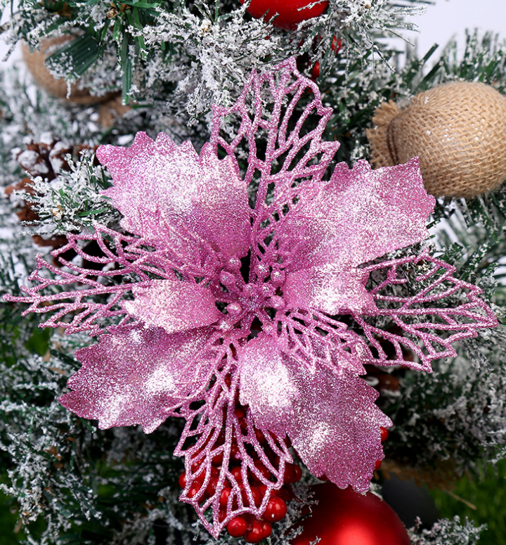 A vibrant pink glittery poinsettia ornament decorates a snow-dusted Christmas tree, accompanied by red berries and burlap accents, embodying festive holiday charm.