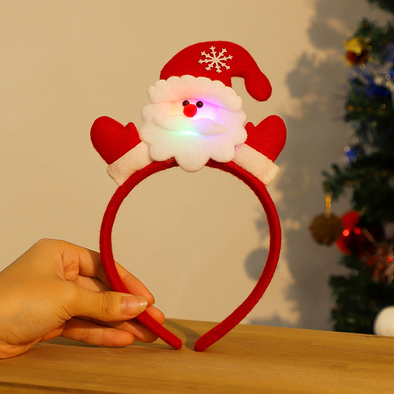 Red headband with a Santa design, featuring a fluffy white beard, red hat, and LED lights. A hand holds it against a blurred background with a decorated tree.
