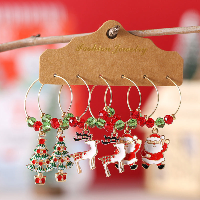 Festive hoop earrings with Christmas-themed charms, including trees, reindeer, and Santa, adorned with red and green beads, displayed on a brown card labeled "Fashion Jewelry."