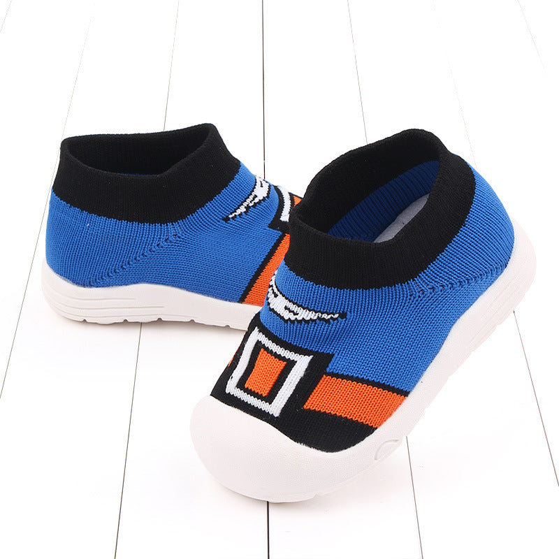 Blue and orange slip-on children's shoes with a cartoon design, featuring white soles and a knit fabric. The shoes are placed on a white wooden floor, one tilted on its side.