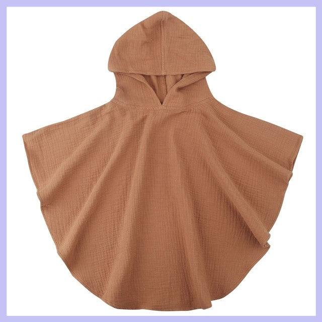 Brown hooded poncho made of textured fabric on a light purple background, spread out to show its loose, flowing shape and simple design.