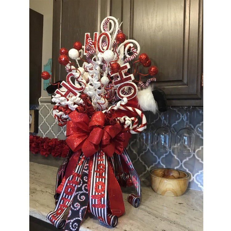 Festive Christmas arrangement with "Ho Ho Ho" signs, glittery red and white swirls, and a large red bow, set against a tiled kitchen backsplash with cabinets above.