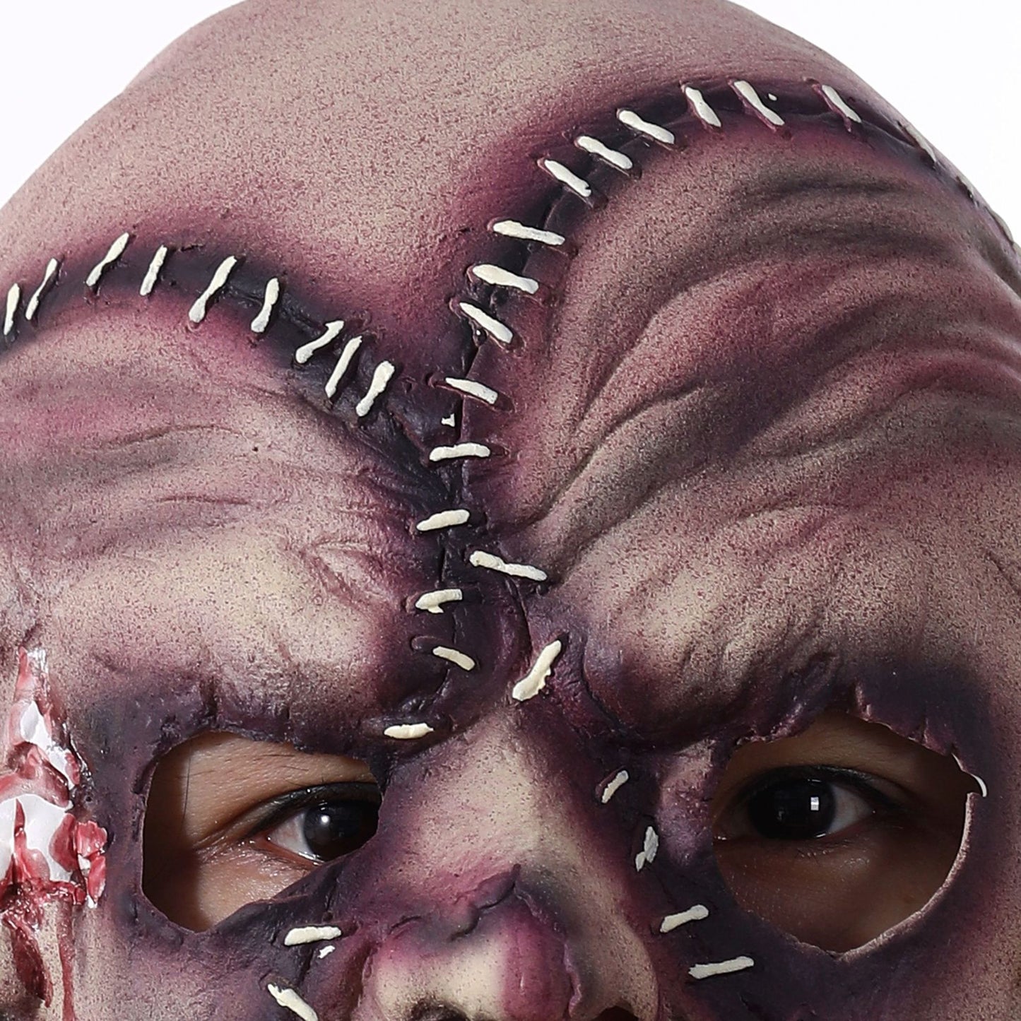 Close-up of a stitched horror mask with white thread and textured skin-like surface, revealing eyes through cutouts. The mask features dark shading and bloodied areas for a realistic effect.