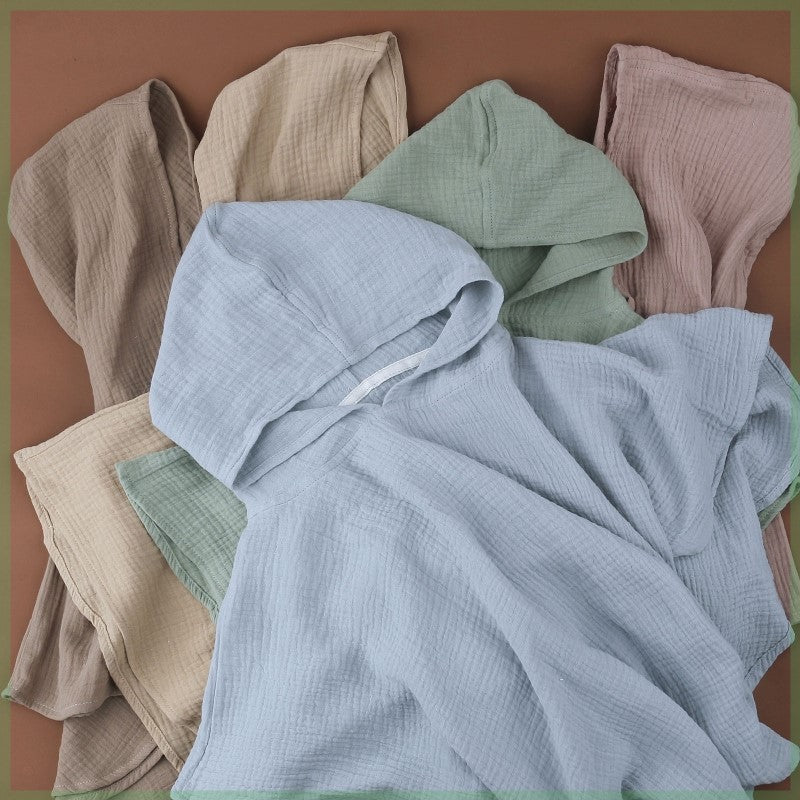 A collection of lightweight, hooded garments in soft pastel shades, including blue, green, beige, and pink, arranged overlapping on a brown background.
