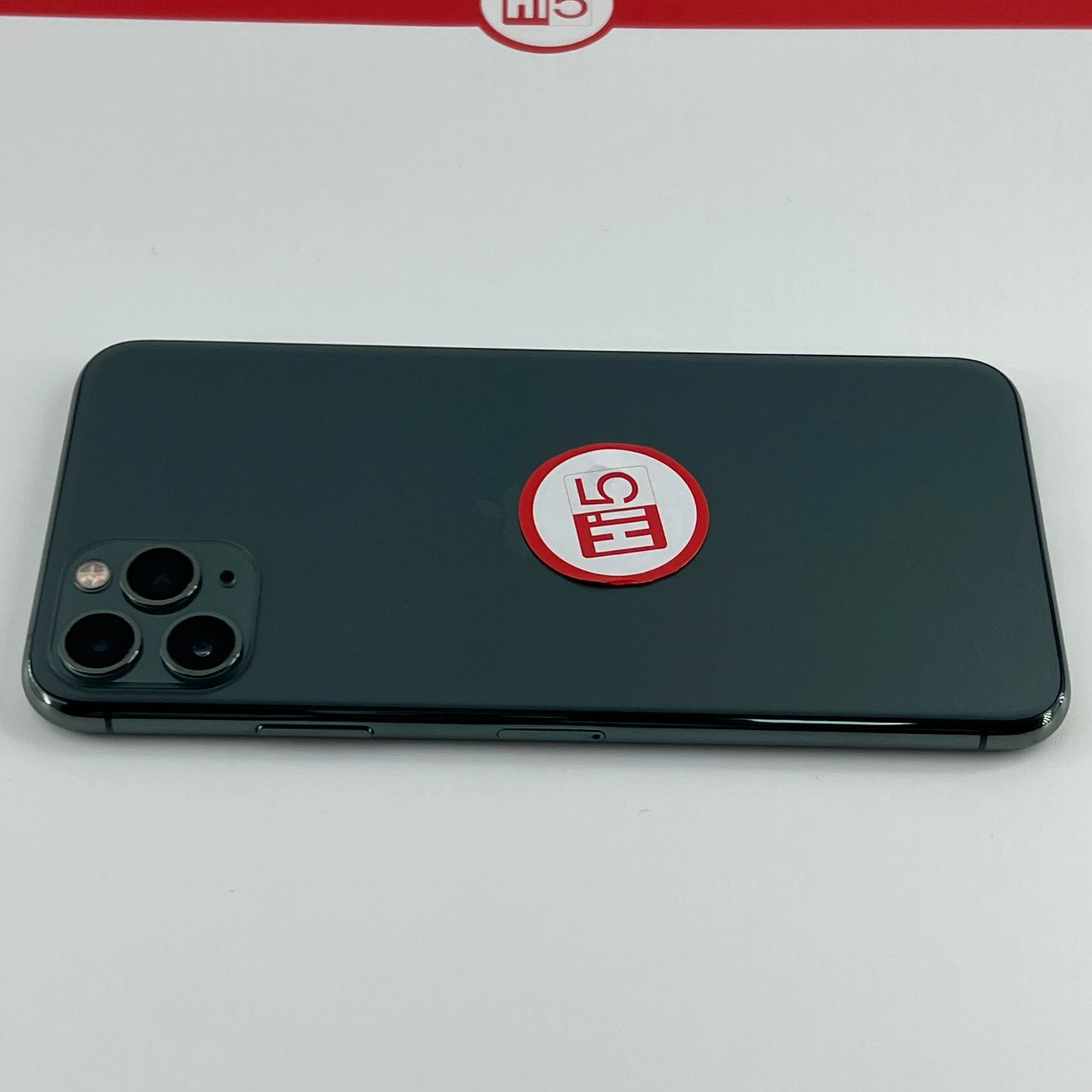 A smartphone with a triple camera setup is placed face down on a white surface, featuring a red and white sticker marked "HI5."