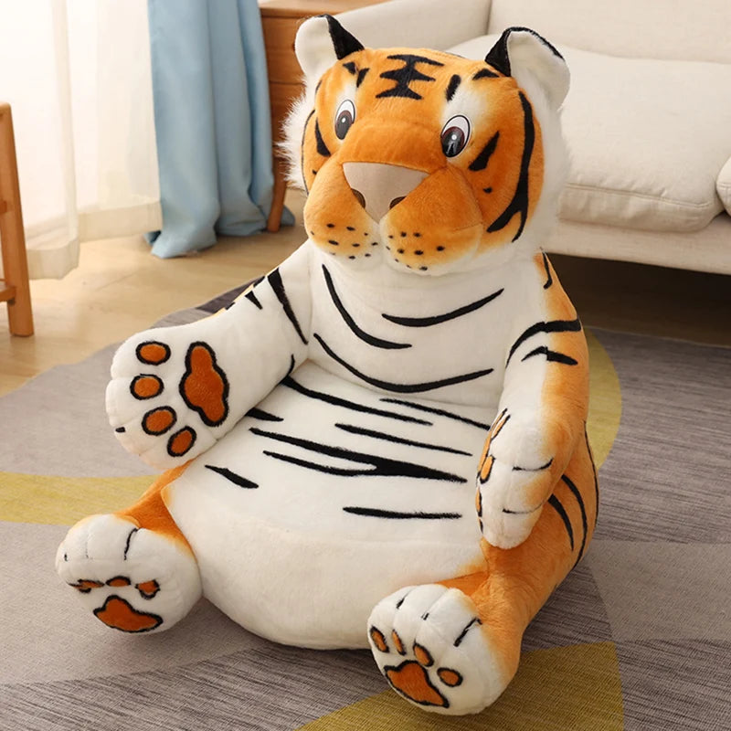 A large, plush tiger cushion with vibrant orange and white fur, black stripes, and friendly eyes, sitting in a cozy living room with a beige couch and light blue curtain in the background.
