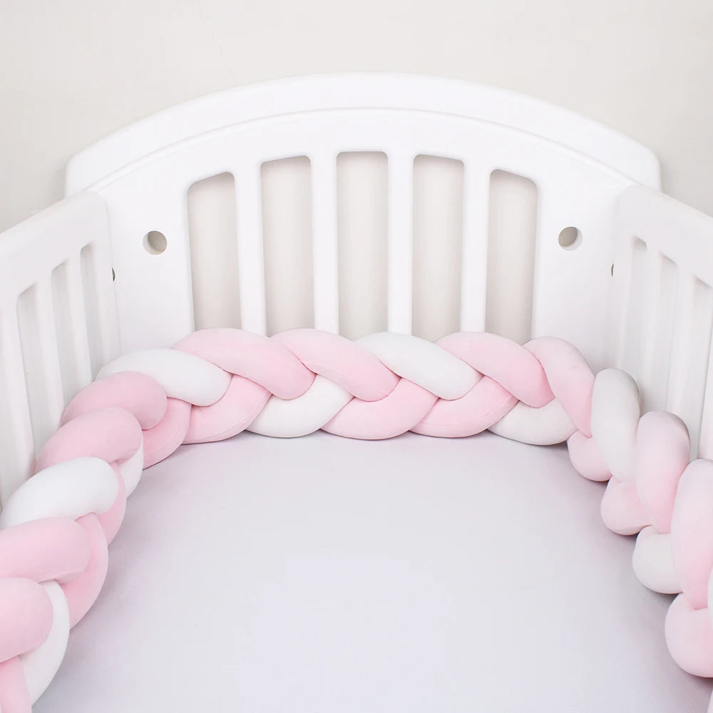 White baby crib with a braided bumper in pink and white colors, providing a soft cushion around the interior.