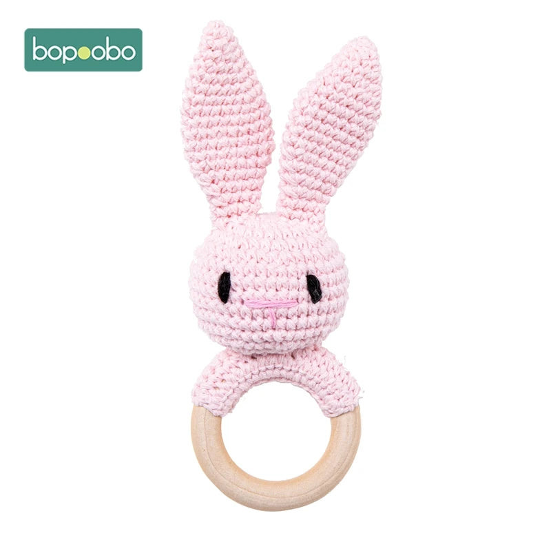 Crocheted pink bunny with long ears attached to a wooden ring. Simple eyes and nose are stitched on its face. The brand logo, "bopoobo," is in the top left corner.