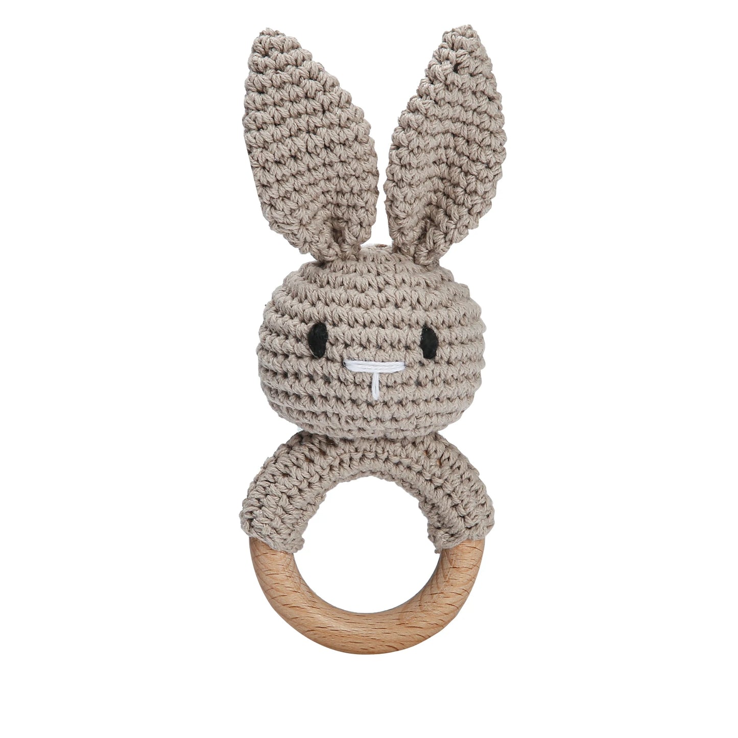 Crocheted bunny rattle with large ears and a smiling face, attached to a wooden ring. The yarn is a neutral beige color, and the design is cute and simple for baby use.