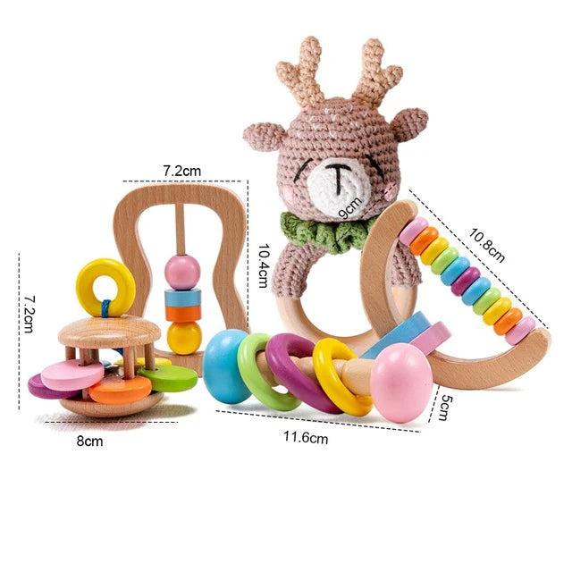 Three colorful wooden baby toys with various shapes and sizes. A crocheted deer toy atop one, a circular rattle with pastel rings, and an abacus with vibrant beads.