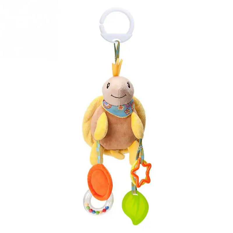 Plush turtle toy with a circular clip, wearing a blue floral scarf, featuring hanging toys: an orange disc, a transparent loop with beads, an orange star, and a green leaf.