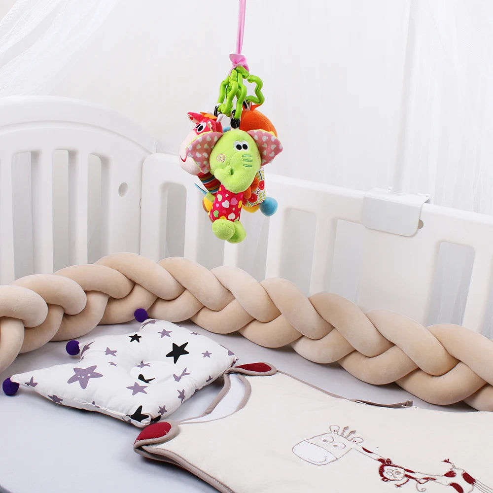 Baby crib with a braided bumper, star-patterned cushion, and a soft toy mobile featuring colorful animals, including an elephant, hanging above.