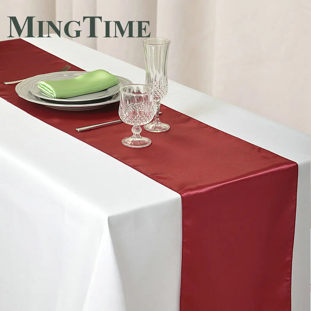 Elegant table setting with a red runner over a white tablecloth, adorned with crystal glasses, silverware, and a white plate topped with a green napkin. "MingTime" logo in the corner.