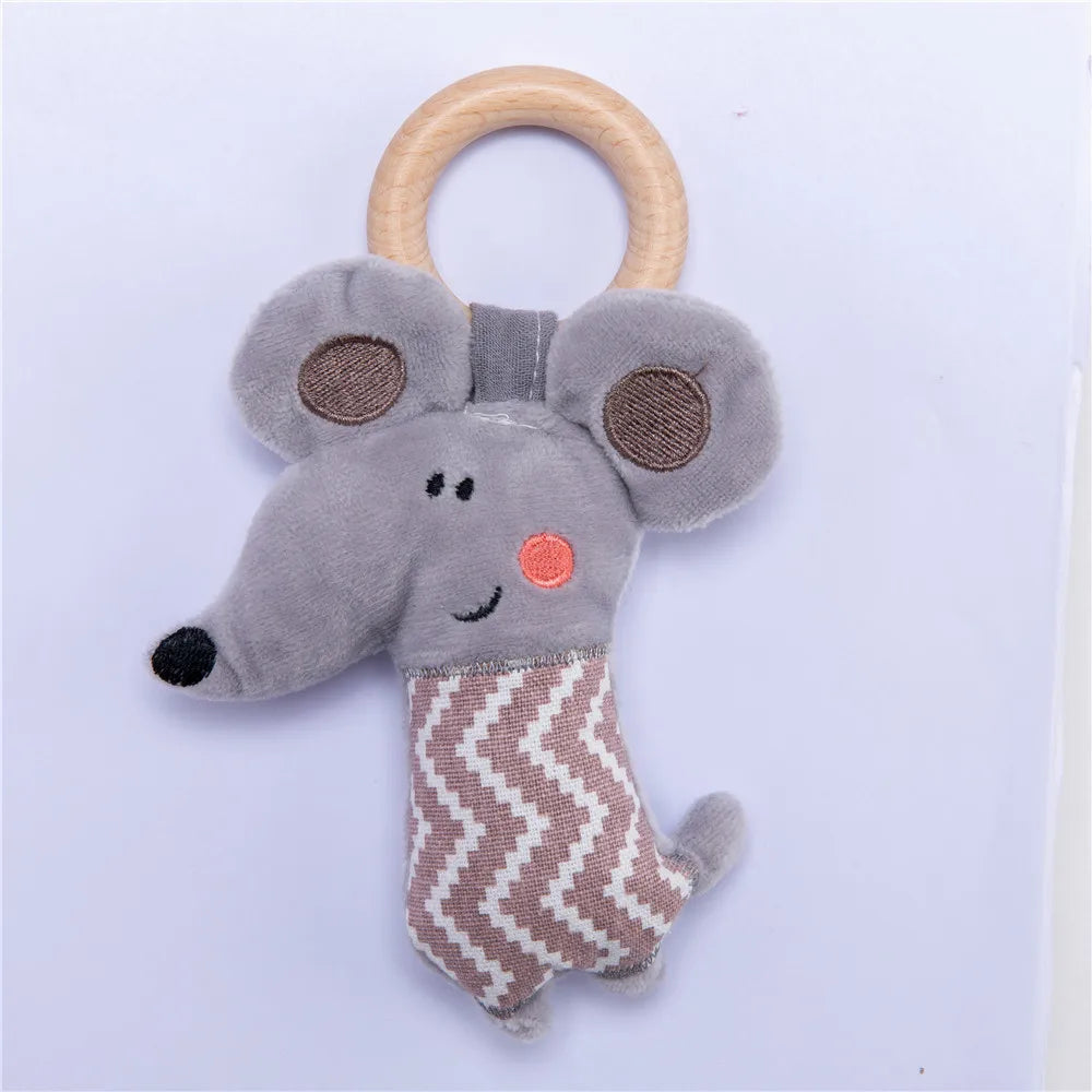 Gray plush toy with large ears, resembling a mouse, attached to a wooden ring. It has a zigzag pattern on its lower half and an embroidered smiley face.