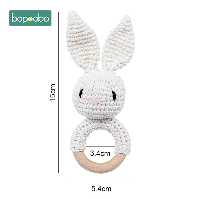 A white crocheted bunny-shaped baby rattle with long ears and a wooden ring handle. Dimensions are labeled as 15cm in height, 3.4cm in head width, and 5.4cm in overall width.