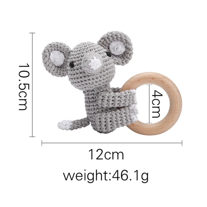 Crocheted gray mouse with large ears holding a wooden ring. Dimensions: 12cm wide, 10.5cm tall, 4cm ring diameter, weighing 46.1g.