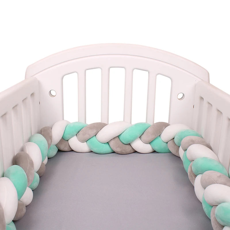 White baby crib with a braided bumper guard in mint, gray, and white colors on a light gray mattress, providing a soft and safe environment for a baby.