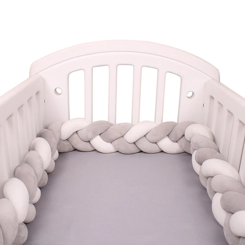 White crib with grey mattress, featuring a soft braided bumper in grey and white colors around the interior edges for added safety and comfort.