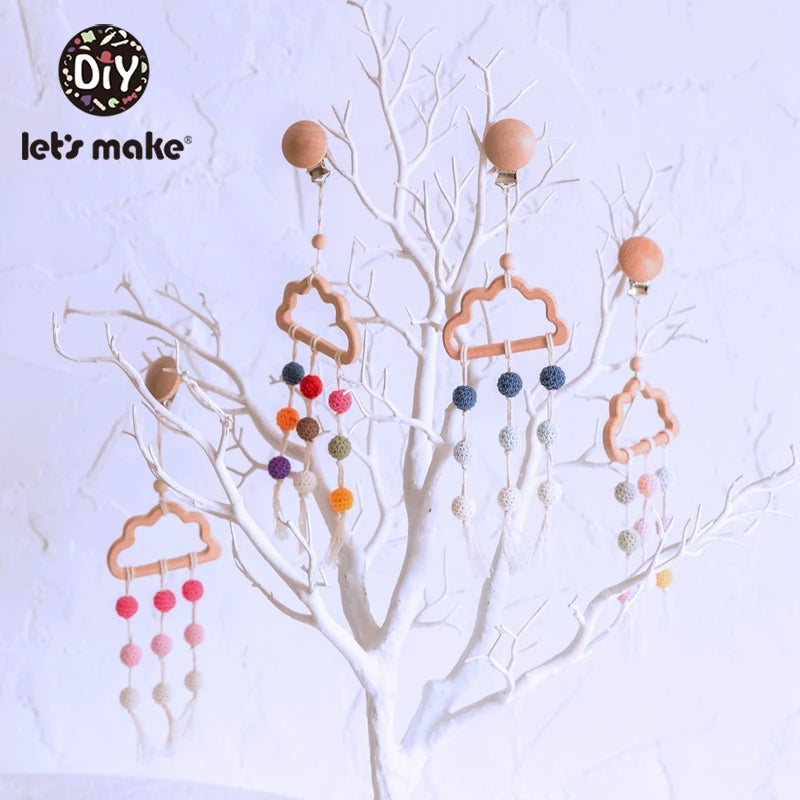 Wooden cloud mobiles with colorful crochet balls hang from a white decorative tree against a light background. The setup includes a logo for a DIY brand.