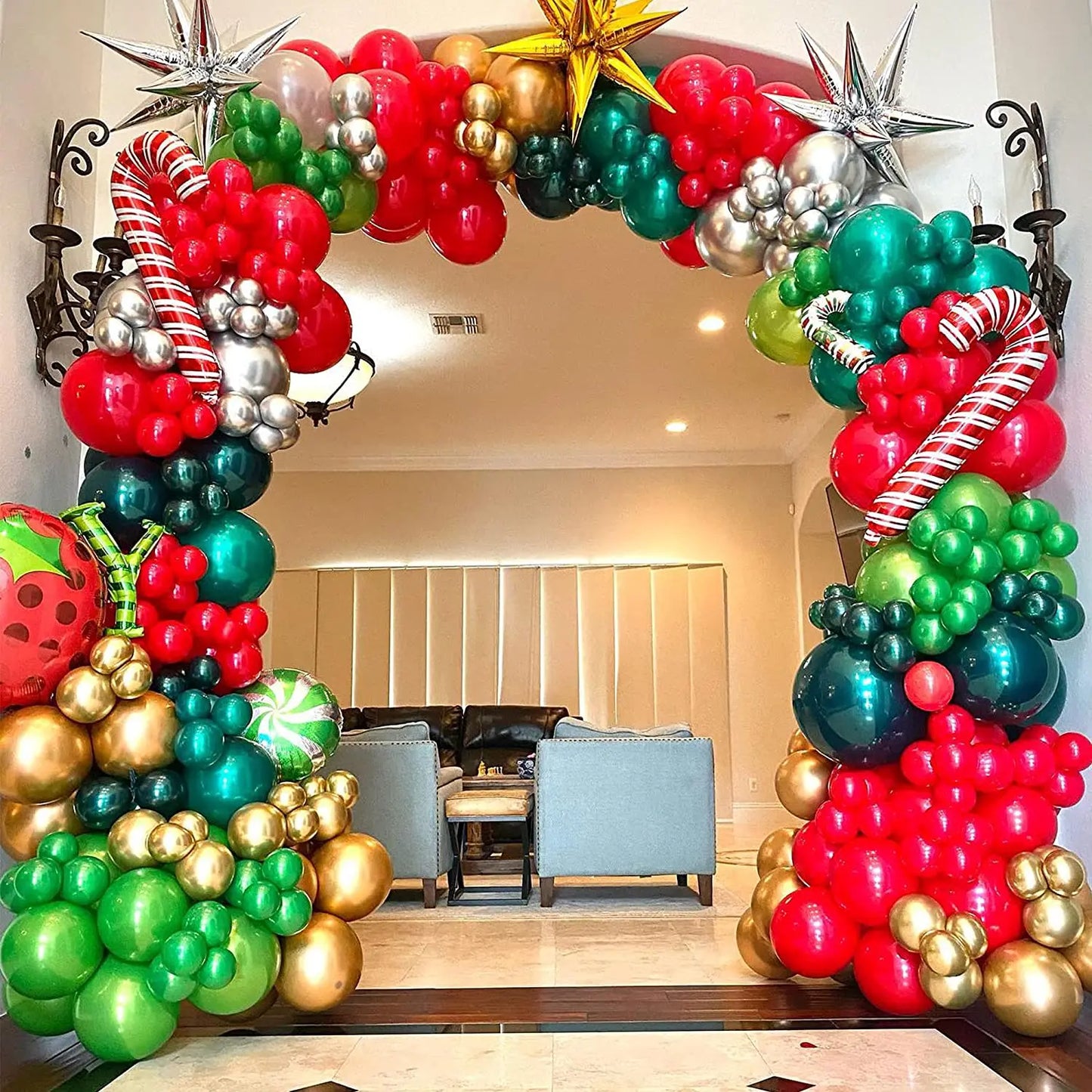 Festive balloon arch with red, green, silver, and gold balloons, candy canes, and star shapes frames a living room entrance, creating a vibrant holiday atmosphere.