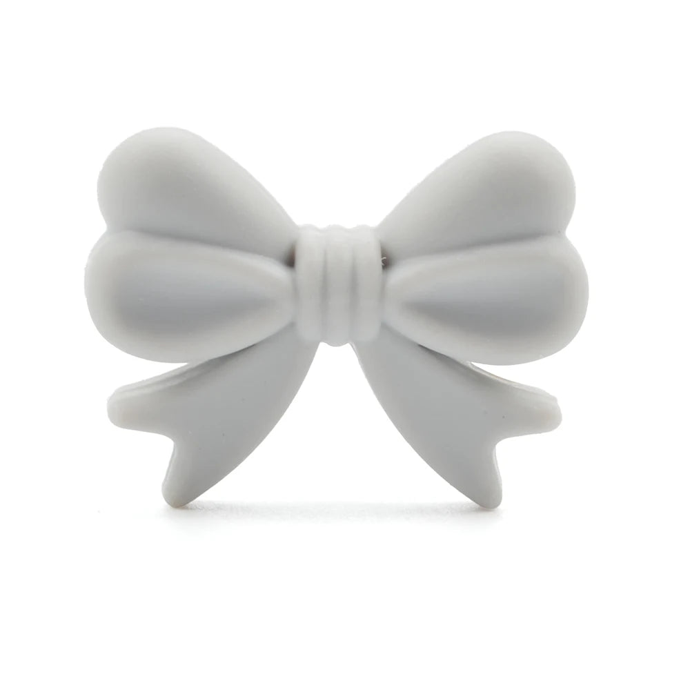 A soft, white bow-shaped teether with smooth, rounded edges and detailed pleats, designed for infants' teething relief against a plain, white background.
