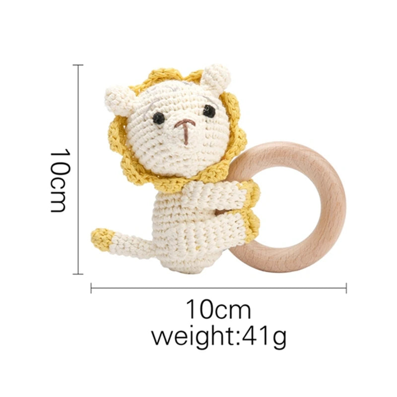 Crocheted lion-shaped baby rattle with wooden handle. The lion is 10 cm tall and weighs 41 grams. It features a yellow mane and a cream-colored body.